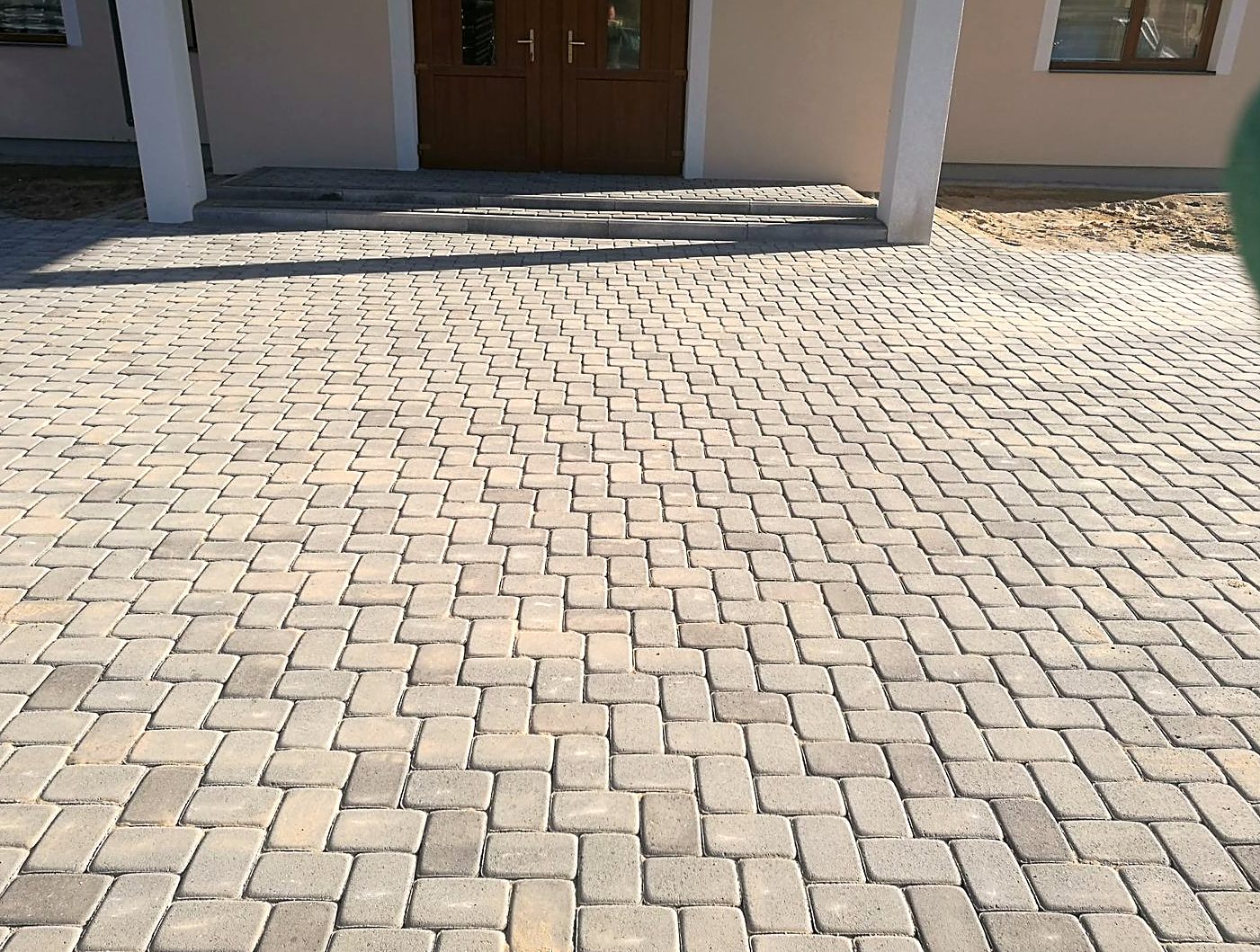 Nobruģēts pagalms ar tumšo lielformāta bruģi un lietus tekni
